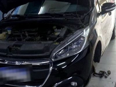 Peugeot con el capot abierto y una rueda desmontada en el taller
